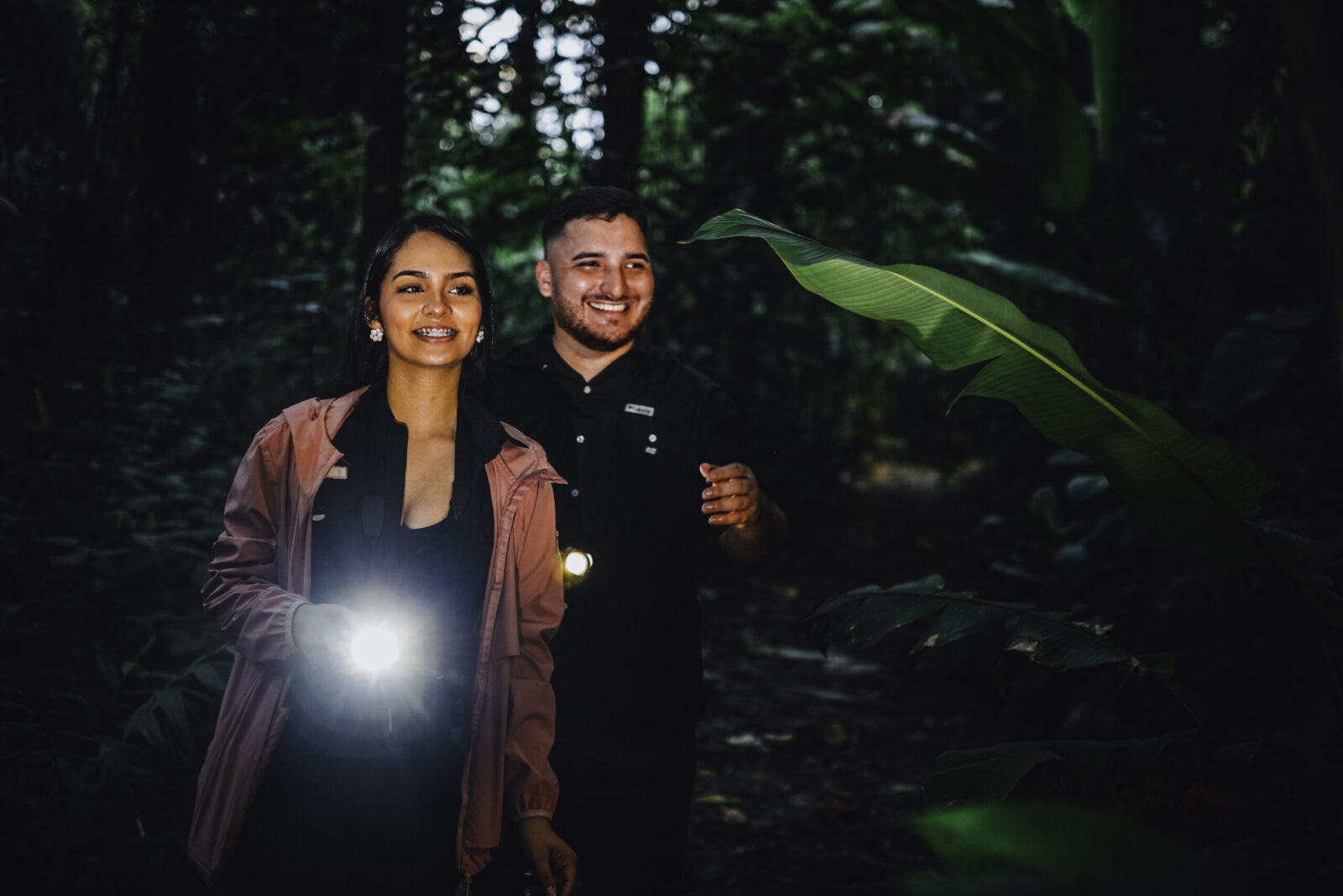 Tourists hiking with a certified guide pointing out nocturnal wildlife on a forest path at twilight in Arenal.